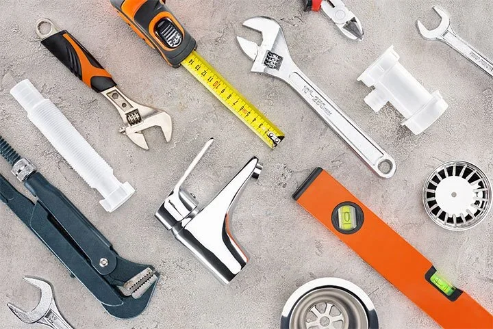 Plumbing tools, fittings, a level, and a measuring tape on a work surface